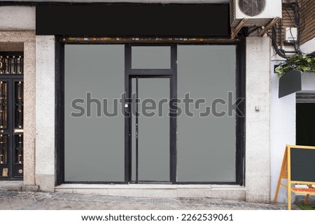 Front of a small street level shop with black metal trim and opaque glass surfaces
