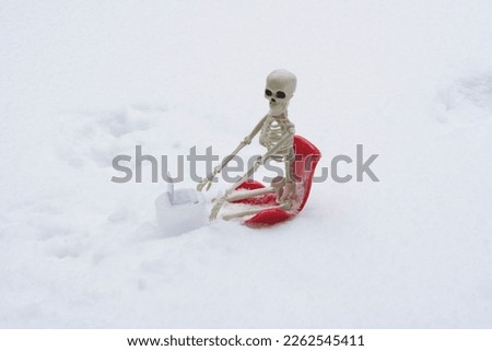 Skeleton sitting in red office chair who has worked so long and so hard that landscape completely covered by snow and snow has fallen on top of laptop covered