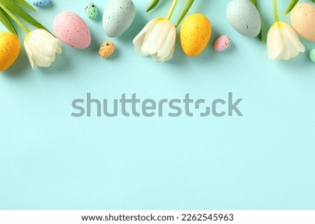 Happy Easter concept. Frame top border made of tulips spring flowers and colorful Easter eggs on light blue background.