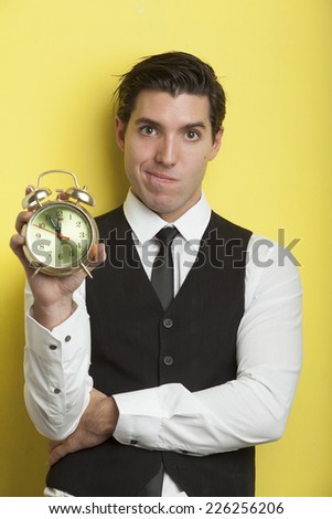 young businessmen on yellow background holding alarm clock stressed out by deadline
