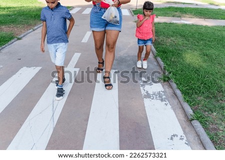 Two kids walking with their mother outdoors in a pathway in a park.