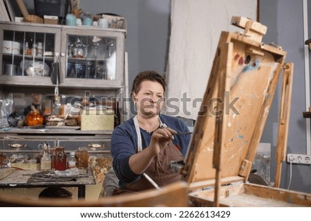 a professional female artist is engaged in painting on canvas in the studio. The artist paints a picture in her studio.