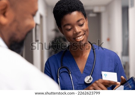 Smiling african american male and female doctor using tablet in hospital corridor. Hospital, medical and healthcare services.