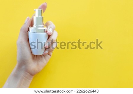 Female's hand holding product of glass bottle with dropper lid on yellow background.Packaging product of cream,lotion,gel, foam or skincare.Cosmetic and medicine product branding mockup.Copy space.