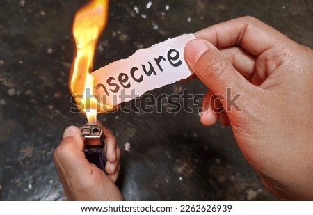 Portrait of a hand burning paper containing the phrase "insecure" with fire, as a symbol that insecure is a negative thought that must be eliminated