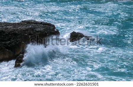 Breaking waves on the coast of Roca Vecchia in Lecce, Italy. Splashing waves of a turquoise blue Adriatic sea crashing against limestone cliffs on a sunny summer day.