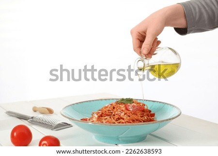 Food stylist pouring oil into spaghetti at white wooden table in photo studio, closeup