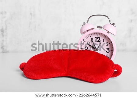 Red sleep mask and alarm clock on white table. Space for text