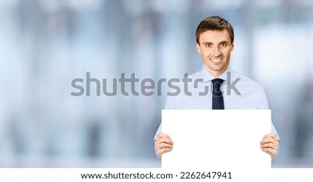 Portrait image of business man professional bank manager in confident cloth necktie holding showing empty white banner signboard paper poster with copy space area. Blurred office background