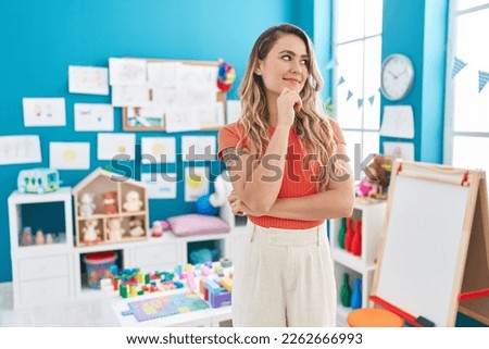 Young caucasian woman working as teacher at kindergarten looking confident at the camera smiling with crossed arms and hand raised on chin. thinking positive.  Royalty-Free Stock Photo #2262666993