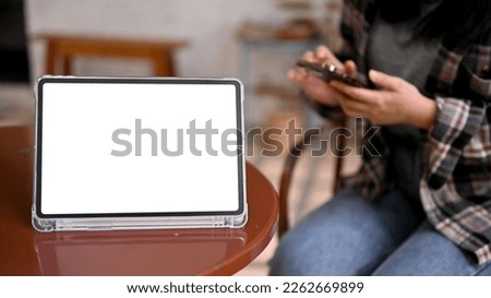 A modern digital tablet white screen mockup for display your graphic stands on a table with a woman sitting beside it. close-up image