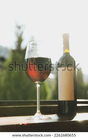 Glass and bottle of red wine on wooden windowsill against mountain background