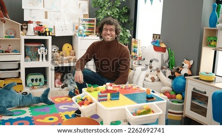 Young hispanic man preschool teacher smiling confident at kindergarten Royalty-Free Stock Photo #2262692741