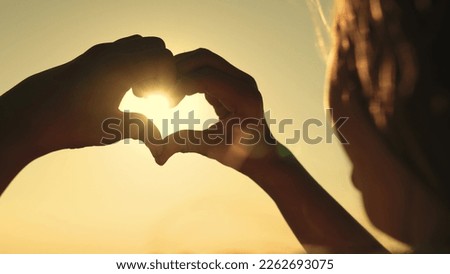 heart sign. girl shows her heart with her hands against backdrop sunset sky. heart made by fingers of the hand in the glare sun. orange sunset. charity gesture. give love. journey beautiful woman.