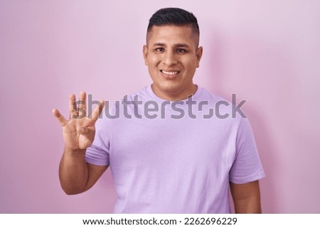 Young hispanic man standing over pink background showing and pointing up with fingers number four while smiling confident and happy. 