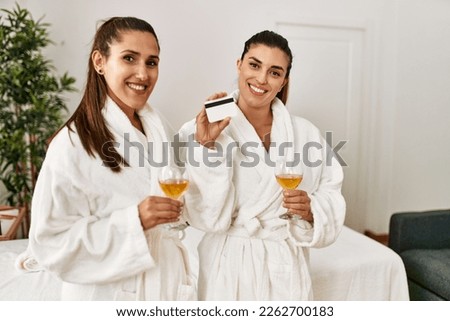 Two women holding credit card toasting with champagne standing at beauty center
