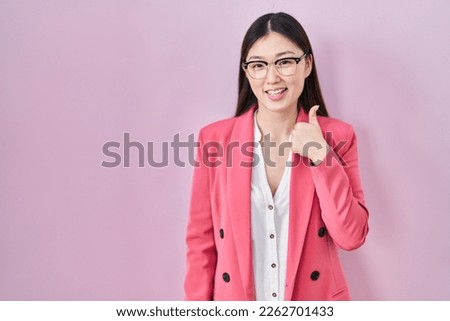 Chinese business young woman wearing glasses doing happy thumbs up gesture with hand. approving expression looking at the camera showing success. 
