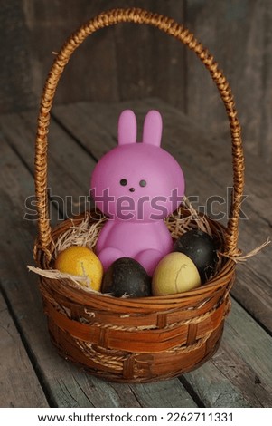 Bunny or rabbit and colorful Esther's eggs in the basket. Adorable small pink rabbit and Esther's eggs on wood background. Rabit standing.