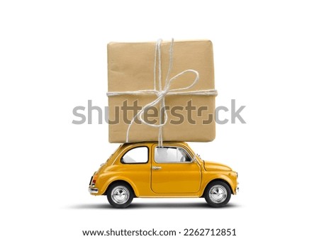 Retro yellow toy car delivering gift box wrapped in kraft paper atop isolated on a white background. Royalty-Free Stock Photo #2262712851