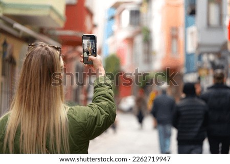 Woman taking photo with phone in the street back view