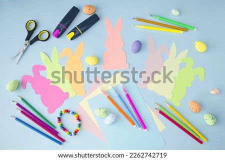 Easter spring holiday.  Craft, children's creativity, cute multi-colored rabbits cut out of paper lie on a blue background.  Flat lay, top view pattern.