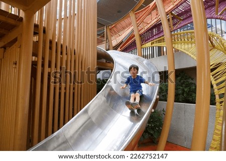 happy asian boy on playground. Kid slide down on slider at plublic playground. Royalty-Free Stock Photo #2262752147