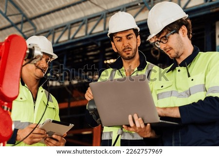 Two technicians workers with safety uniform using laptop talking and controlling machinery at manufacturing area of industrial factory