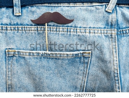 Man's mustache on a wooden stick in a denim pocket. Concept barber shop background with mustache.