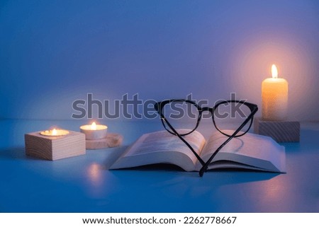 Eyes glasses and Holy Bible with candles lighting on blue background. Variative focus.