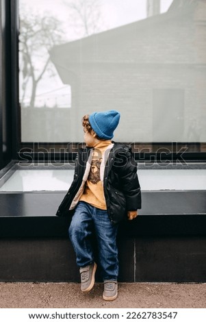 Toddler boy, outdoors,sitting on glass wall background.