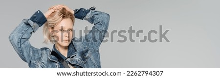 blonde woman in stylish denim jacket posing with hands on head isolated on grey, banner
