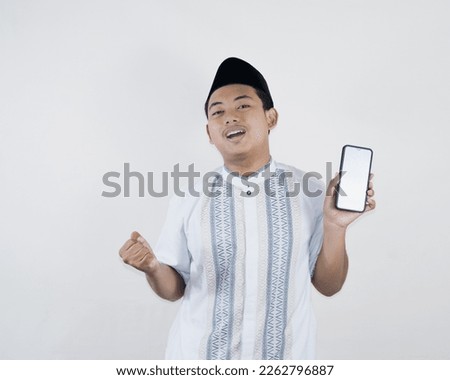 Young muslim man smiling and happy with what he sees on smartphone. Indonesian youth on a white background.