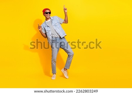Full length photo of cheerful cool guy dressed denim clothes dark eyewear pointing empty space isolated yellow color background