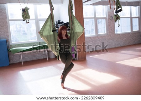 Happy active middle-aged woman 40s years old  on hammock practice fly yoga stretching in fitness club, do sports exercise training workout follow healthy lifestyle. Fly antigravity yoga