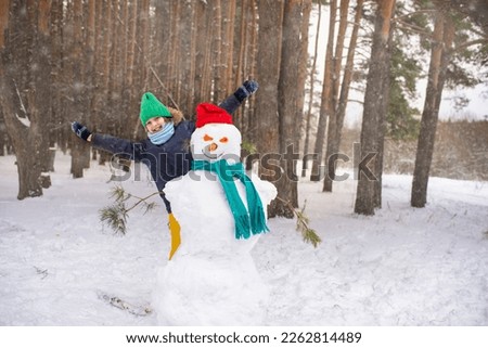 a boy peeks out from behind a snowman, a happy child plays hide and seek in the winter forest