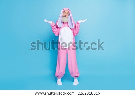 Full size photo of uncertain elderly pensioner wear pink bunny costume shrugging shoulders have no idea isolated on blue color background
