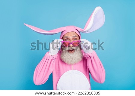 Photo of positive impressed retired guy wear pink hare sleepwear hands arms heart glasses isolated blue color background