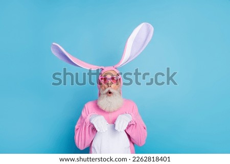 Photo of excited fooling man pensioner dressed pink rabbit nightwear heart eyewear rising arms hands isolated blue color background
