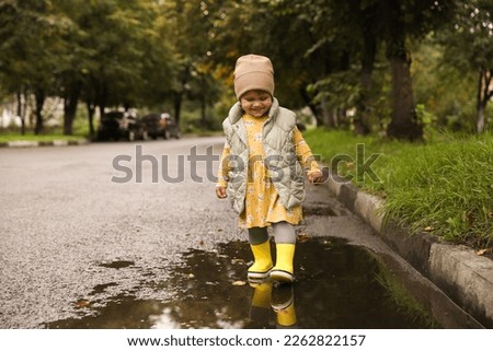 Cute little girl splashing water with her boots in puddle outdoors, space for text