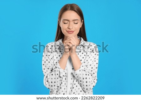 Woman with clasped hands praying on turquoise background Royalty-Free Stock Photo #2262822209