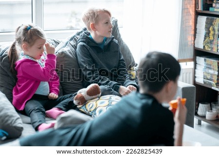 Group of children sitting on sofa in living room, watching TV interesting film movie cartoon, spending free time together on sunny day. Childhood, entertainment, siblings, relationship, friendship. 