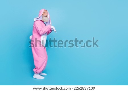 Full length photo of positive fooling man pensioner dressed pink rabbit nightwear jumping empty space isolated blue color background