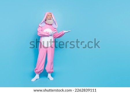 Full length photo of dreamy funny retired guy wear pink hare sleepwear showing arms empty space isolated blue color background
