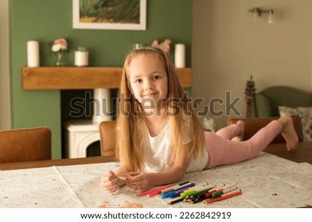The girl paints an Easter picture lying on the table in a bright interior