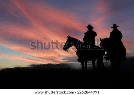 Two cowboys in silhouette on horseback at first light