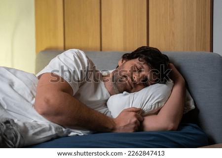 Sleeping young man, peacefully resting in a comfortable bed, lying with his eyes closed. The concept of time for rest and nap.  Royalty-Free Stock Photo #2262847413