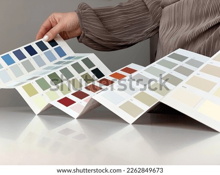 Close-up of interior designer woman choosing samples of wall paint. Concept: interior designer looking at color swatch for creating project