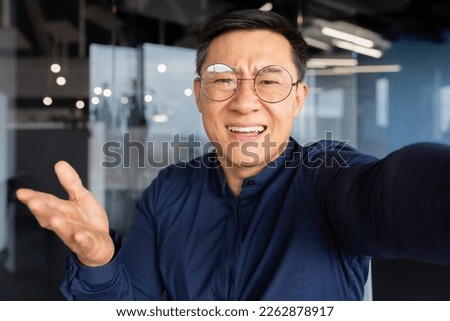 Angry and grumpy asian businessman talking on video call, man inside office looking at smartphone camera, boss in casual shirt shouting at camera. Royalty-Free Stock Photo #2262878917