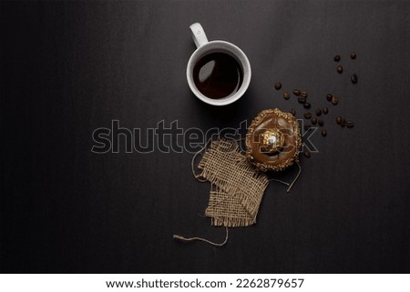 coffee composition, aerial shot of a white ceramic mug filled with black coffee, on the side a cupcake donut, coffee beans and a straw weaving. Space for content