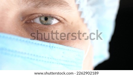 Half face of a doctor in a mask on a black isolated background. The doctor looks into the camera on a black background. Handsome doctor man with a serious look.